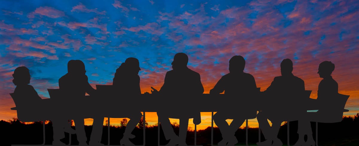 Header Image: People sit at a board room table against a sunset background